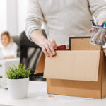 Homem recolhendo seus pertences na mesa de trabalho pois foi demitido.