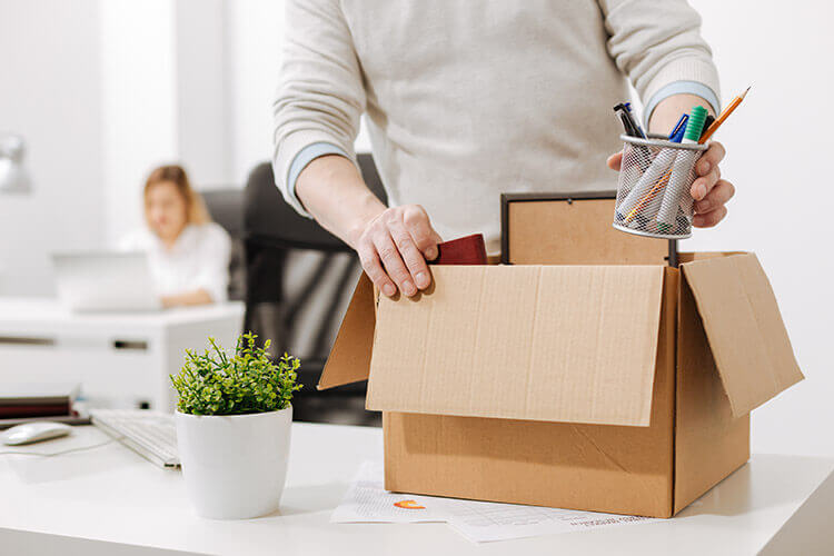 Homem recolhendo seus pertences na mesa de trabalho pois foi demitido.